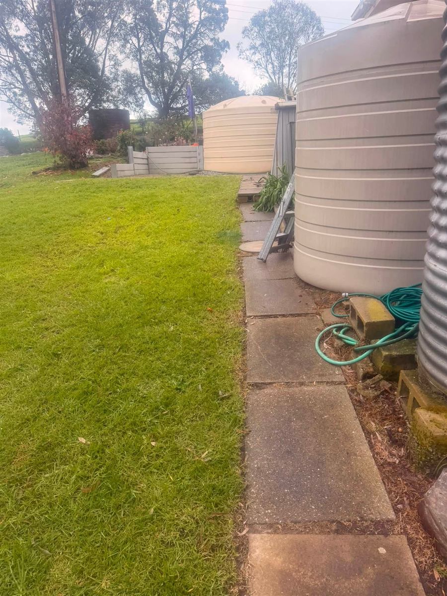 Side lawn mowed beside a water tank and paved path in Normanville